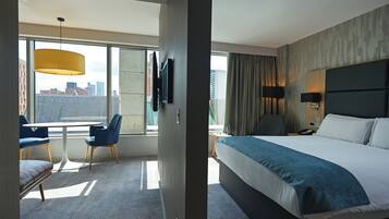 Een moderne hotelkamer met een groot bed, een bureau met stoelen, een televisie en uitzicht op de stad.