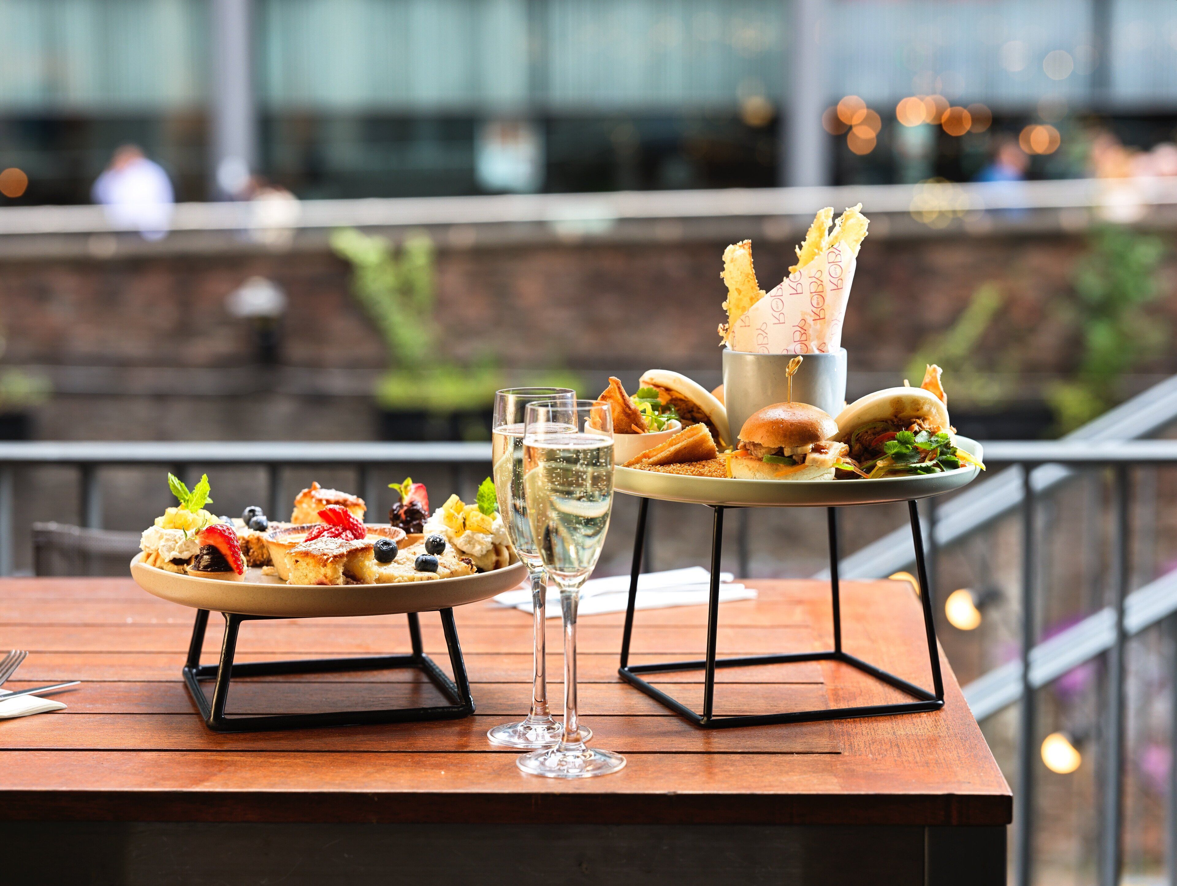 A dining table with a variety of dishes and drinks, set against a blurred outdoor background.