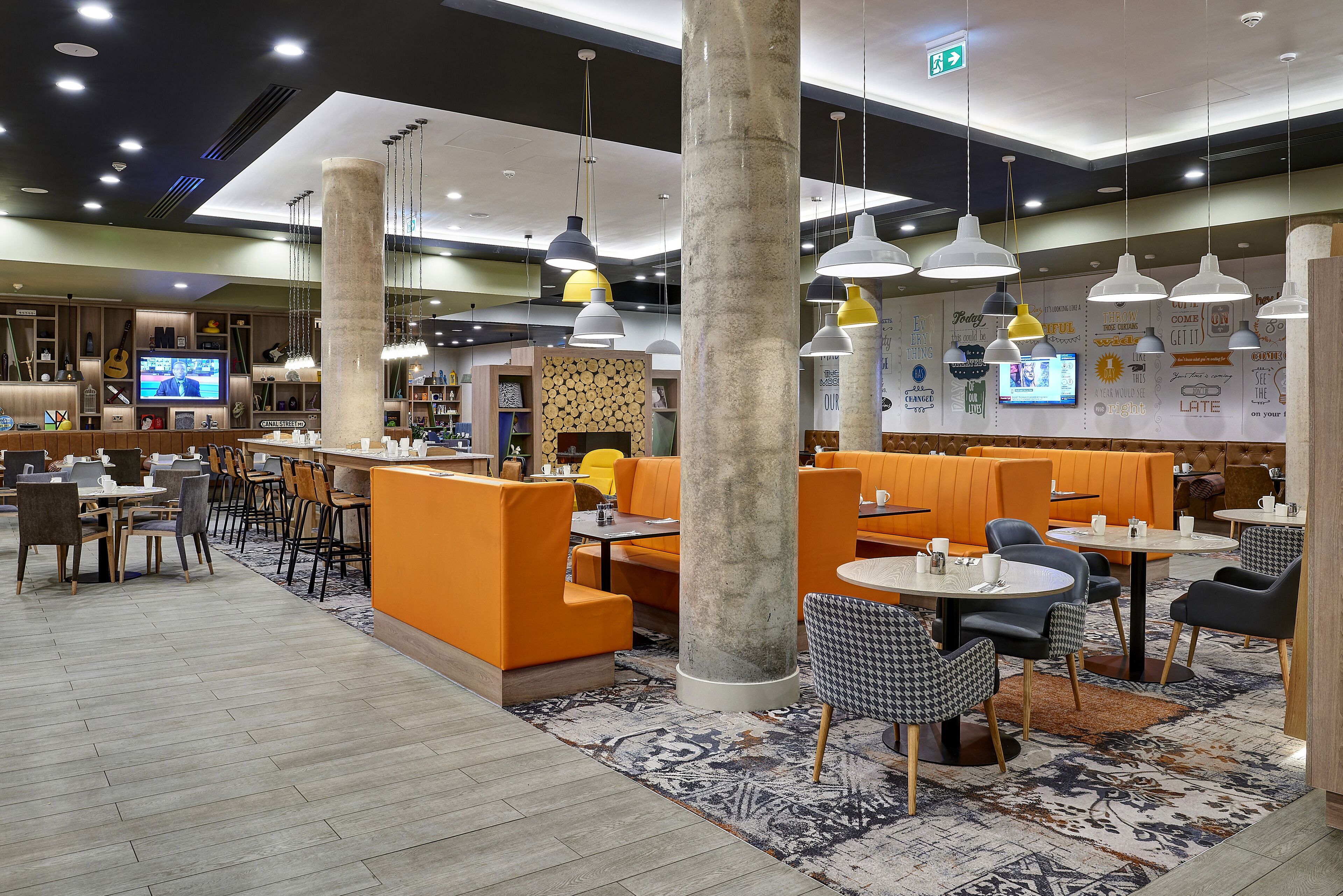 Un restaurant moderne avec des banquettes orange, des tables rondes et des suspensions lumineuses.