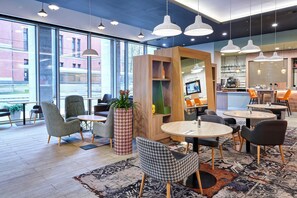 A modern cafe with round tables and chairs, large windows, and a bar area. - Holiday Inn Manchester - City Centre by IHG (Manchester)