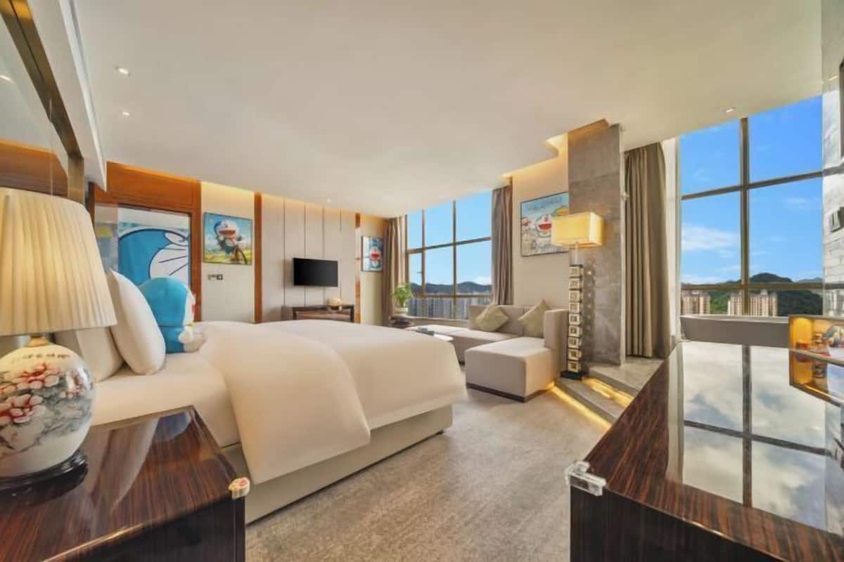 A modern hotel room with a large bed, a sofa, a desk, and a TV.