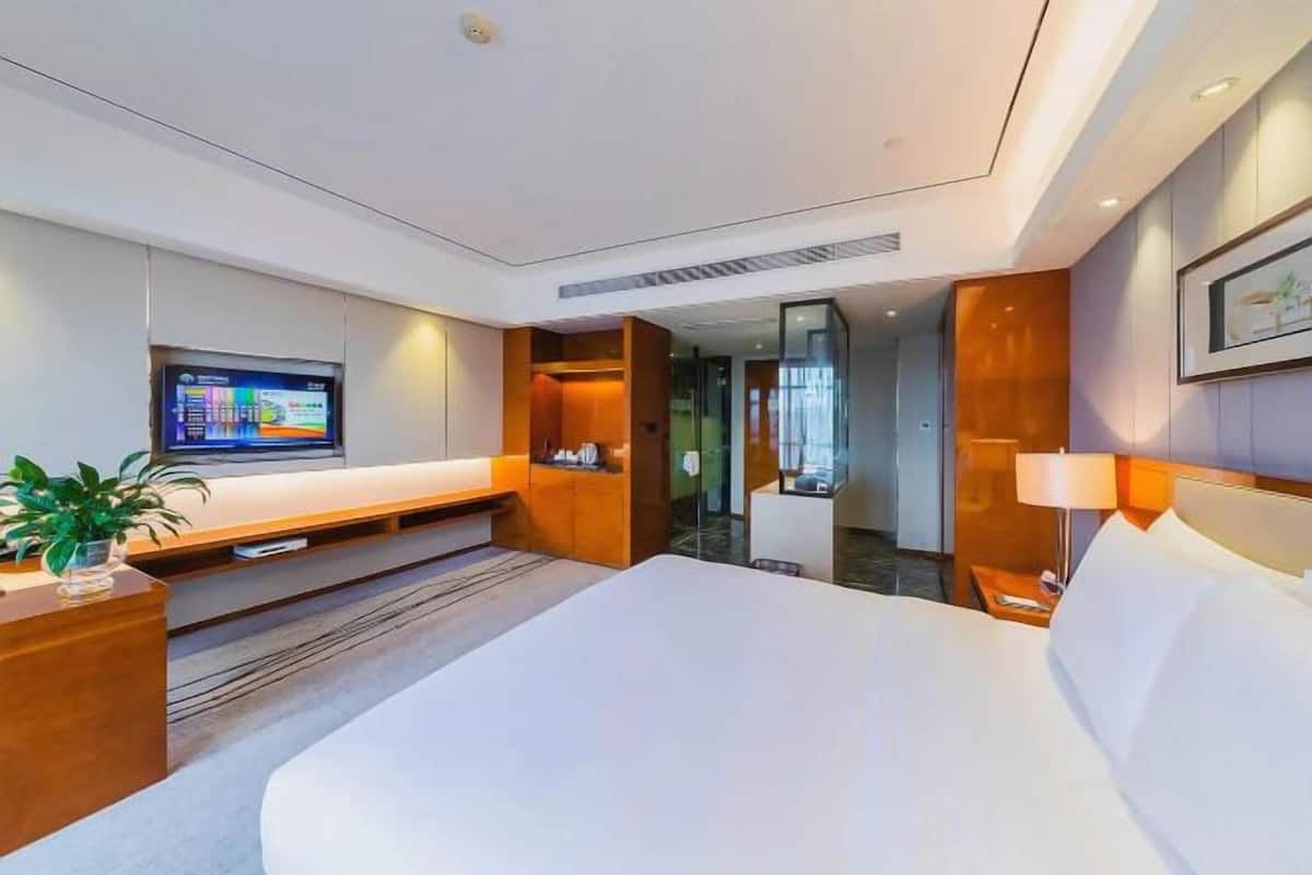 A modern hotel room with a large bed, a flat-screen TV, a desk, and a seating area.