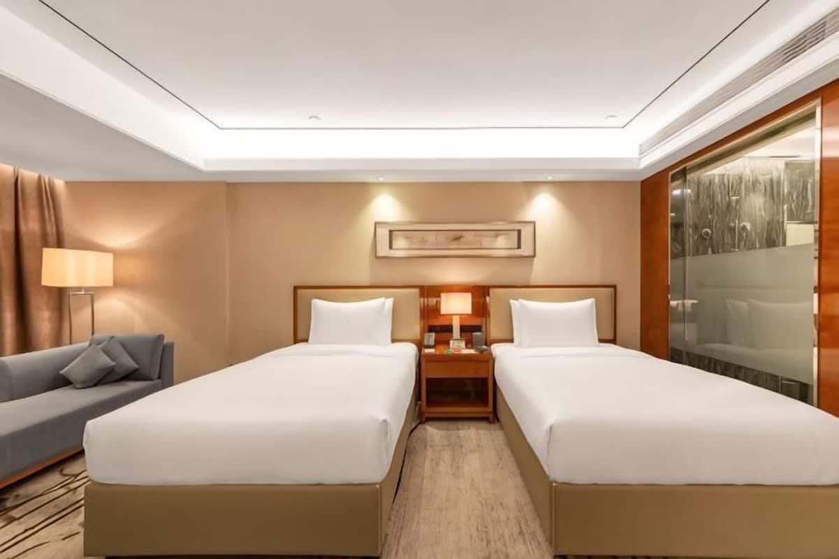 A hotel room with two beds, a sofa, a nightstand with a lamp, and a large window.