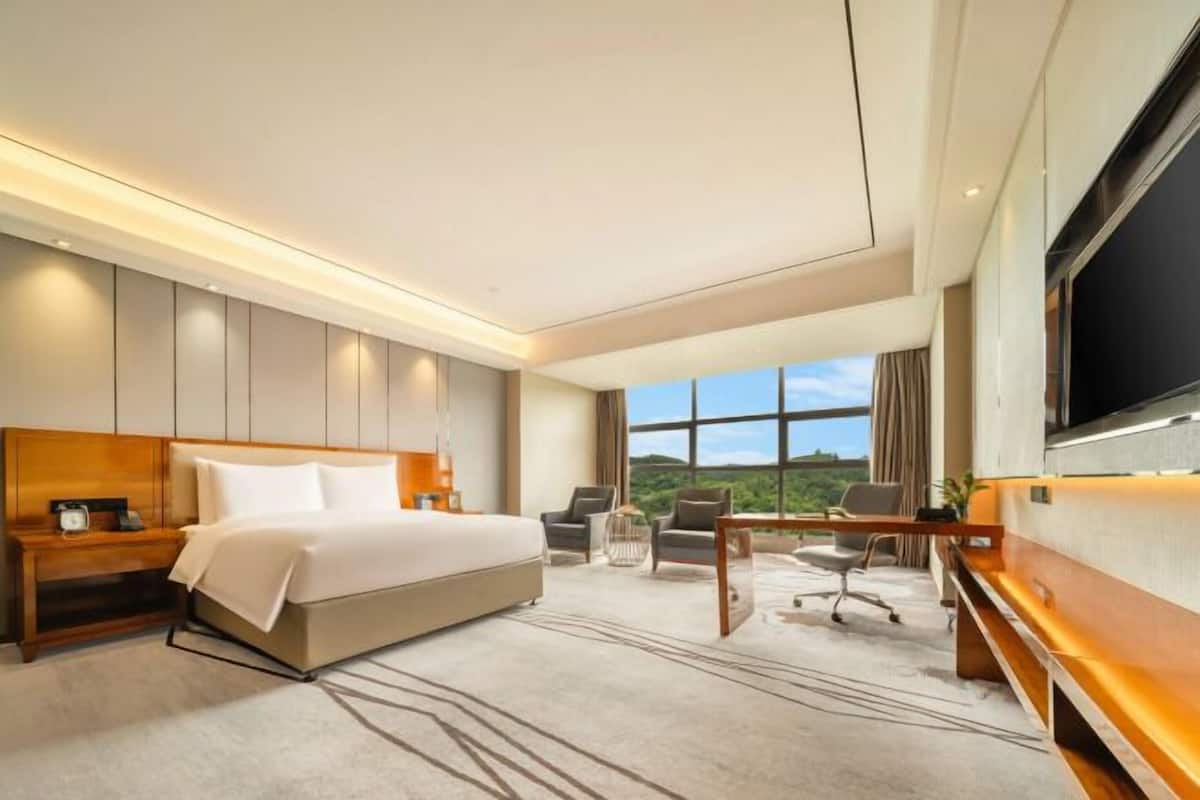 A modern hotel room with a large bed, a desk, a chair, and a television.