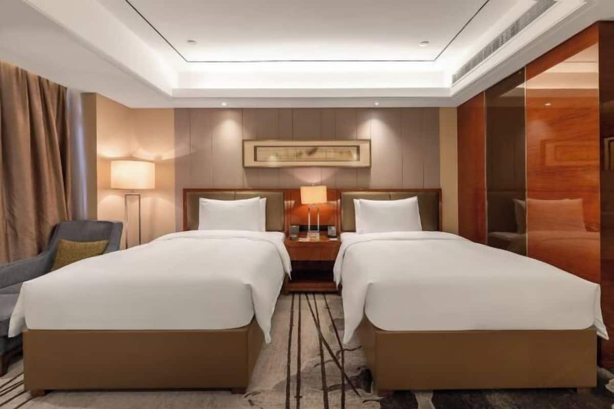 A hotel room with two beds, a desk, a chair, a lamp, and a painting on the wall.