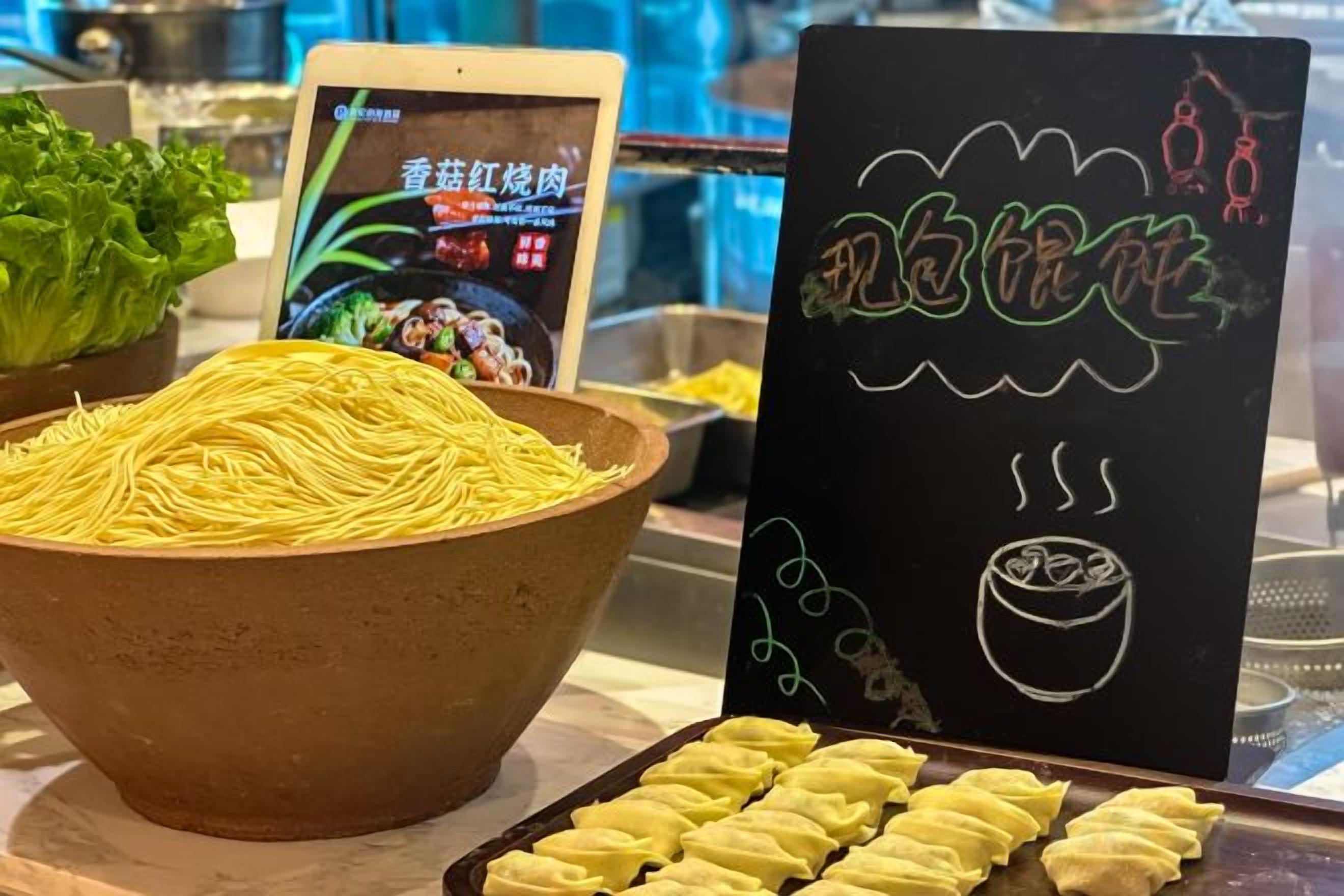 A bowl of noodles, a smartphone displaying a food-related app, and a chalkboard menu with Chinese characters.