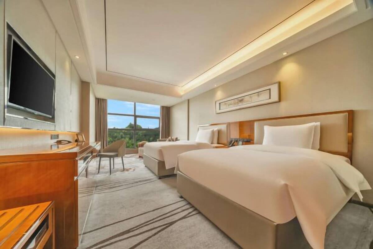 A hotel room with two beds, a desk, a TV, and a view of the outdoors.