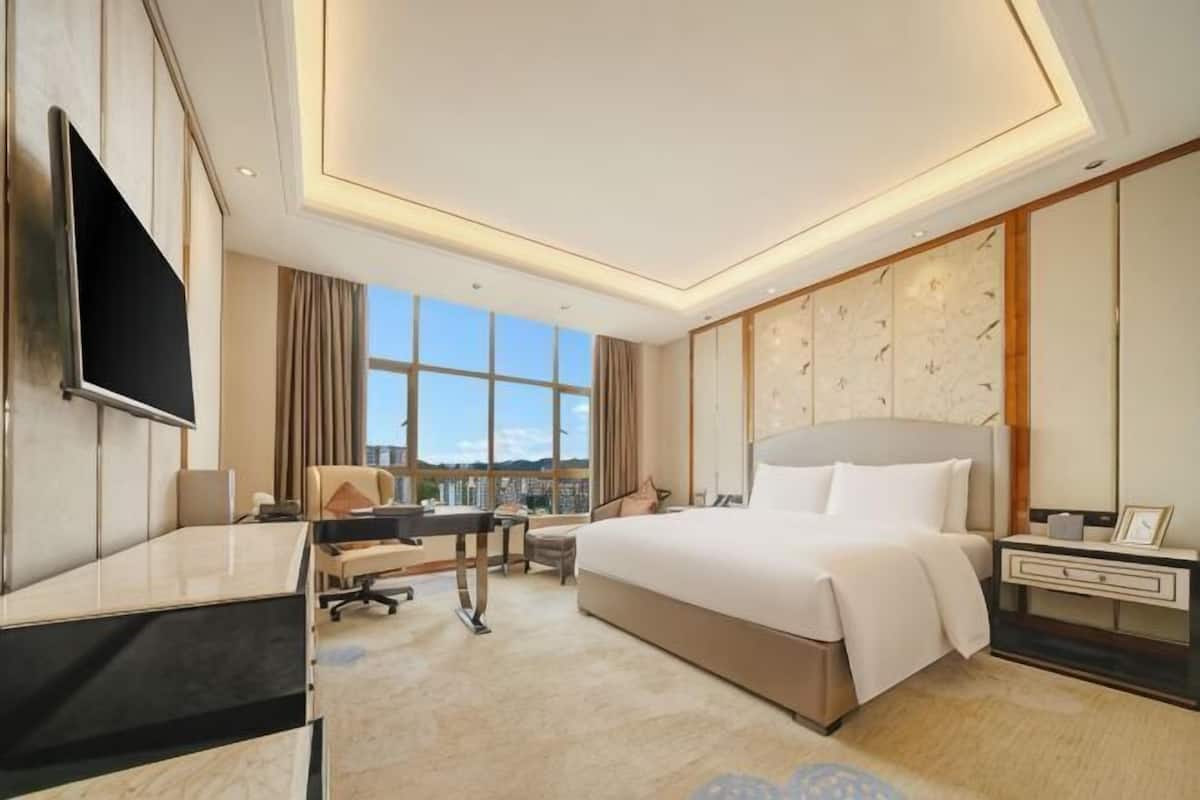 A hotel room with a large bed, a desk, a TV, and a city view.