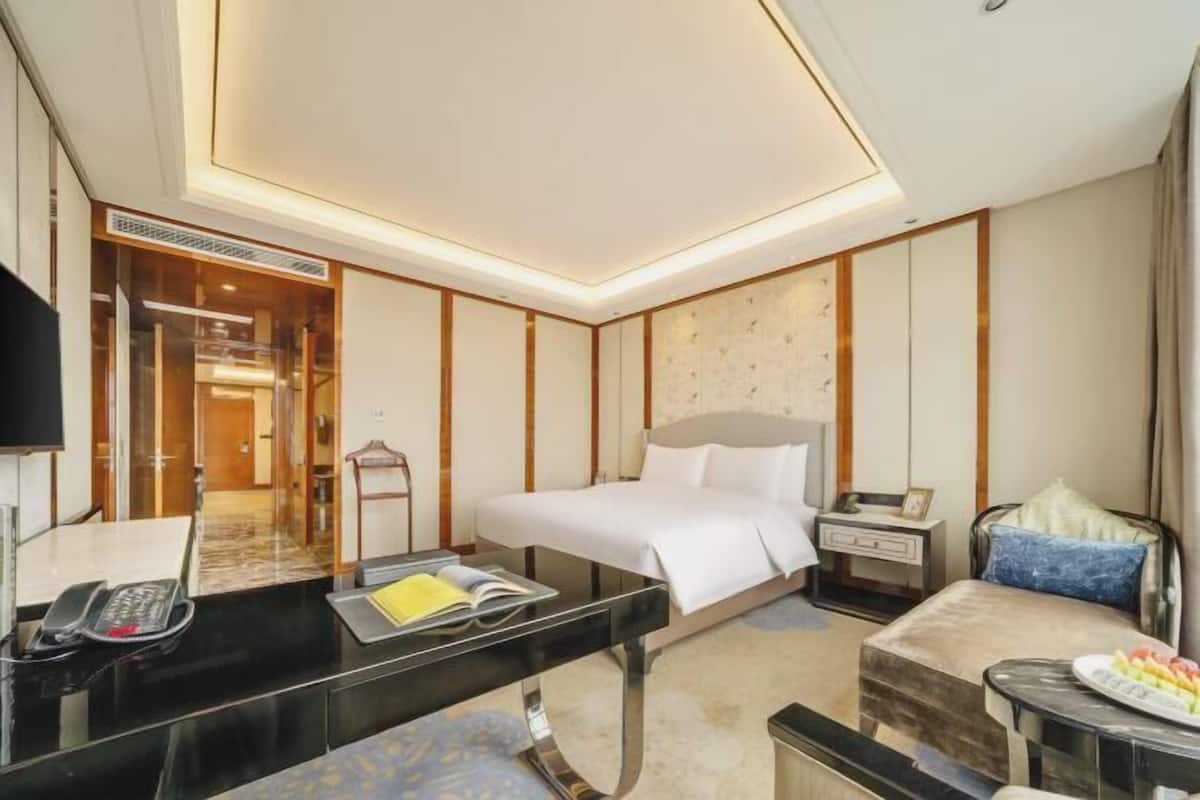 A hotel room with a bed, bedside table, chair, desk, and a small table with a plate of fruit.