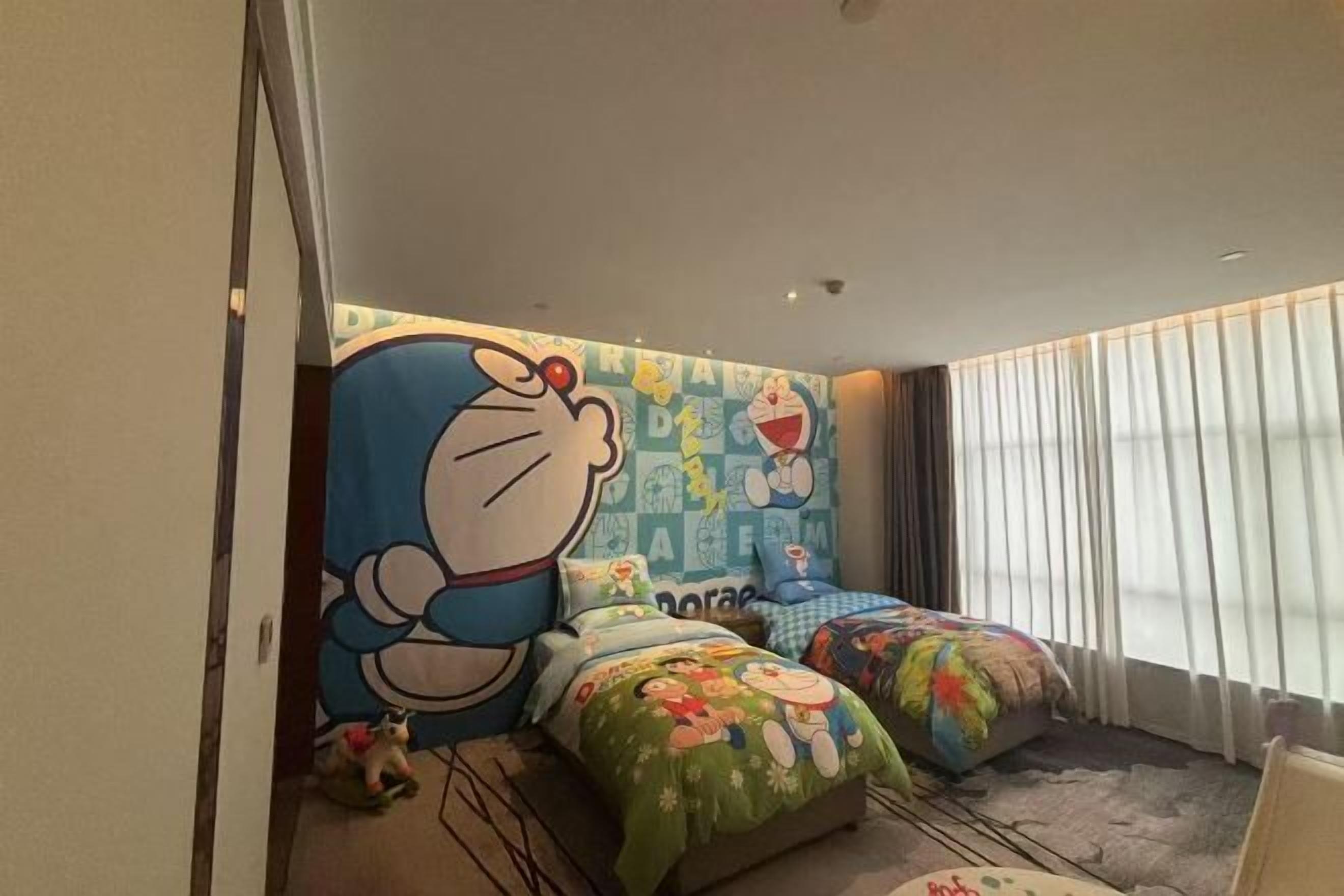 A bedroom with two beds, a large cartoon character mural on the wall, and a window with curtains.