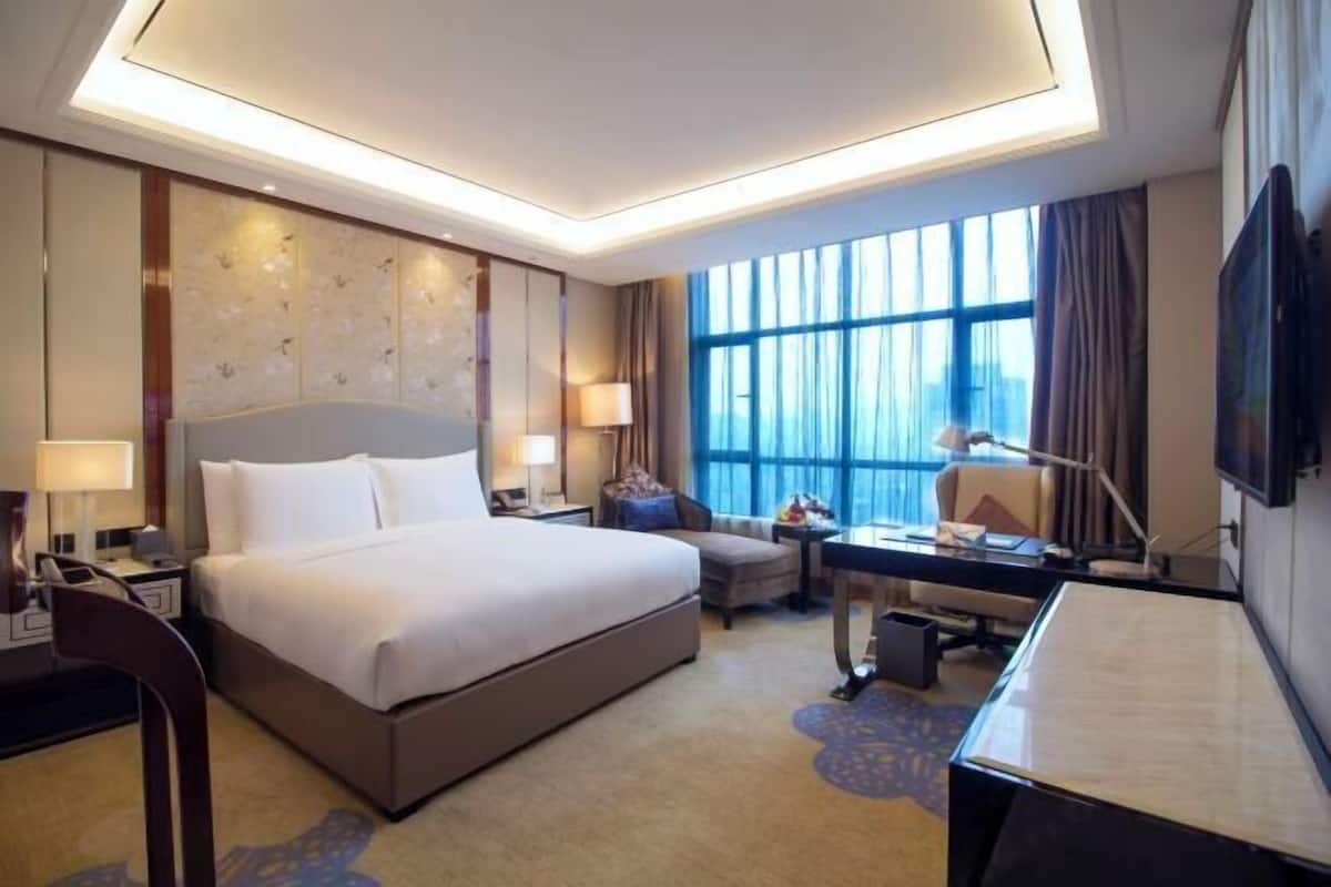 A hotel room with a large bed, a desk, a chair, a TV, and a window with curtains.