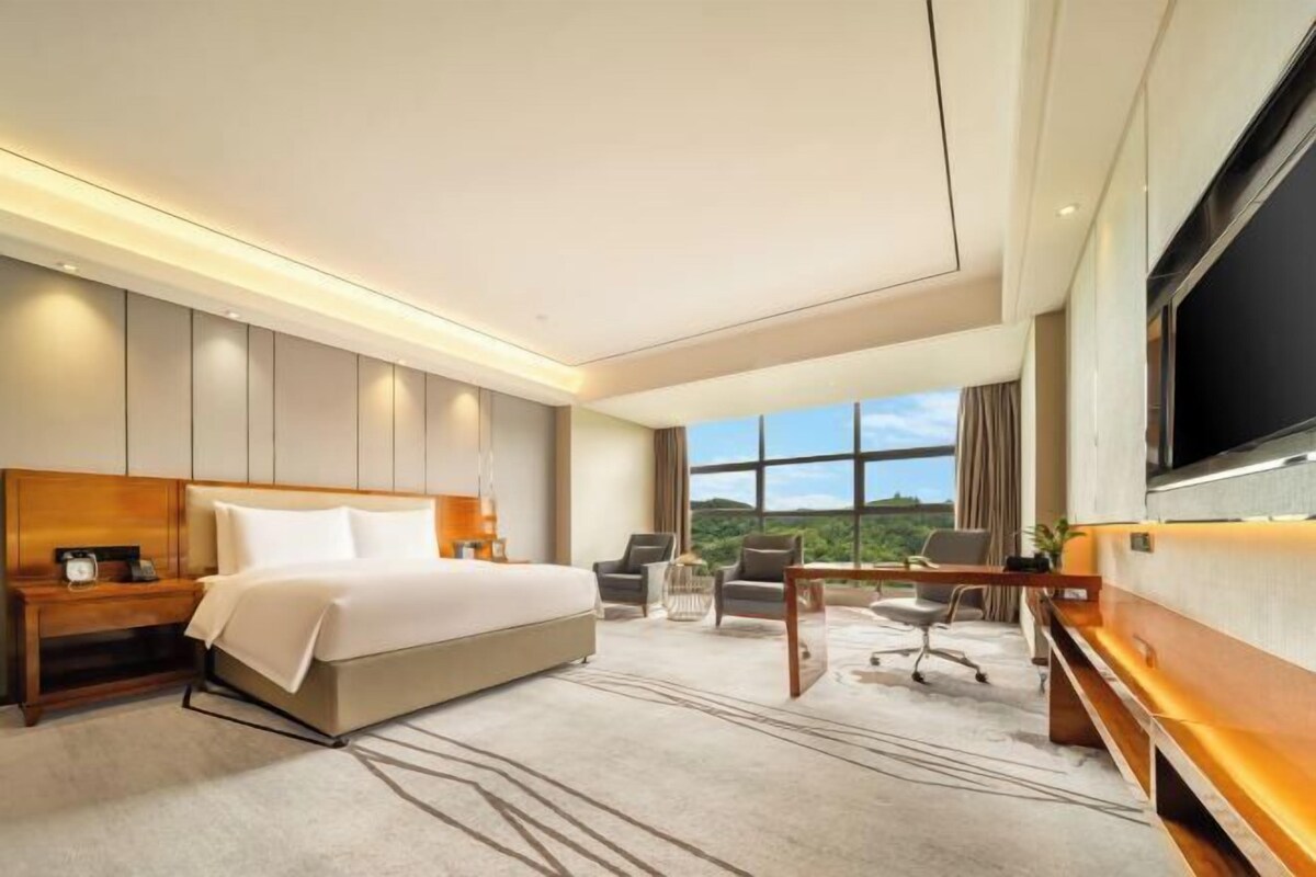 A modern hotel room with a large bed, a desk, and a TV.