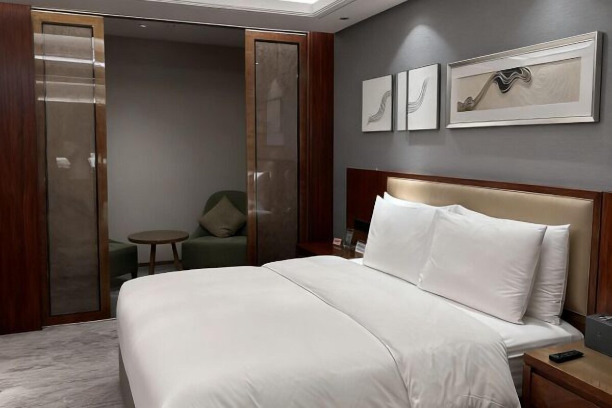 A hotel room with a bed, a nightstand, a chair, a small table, and a sliding door.