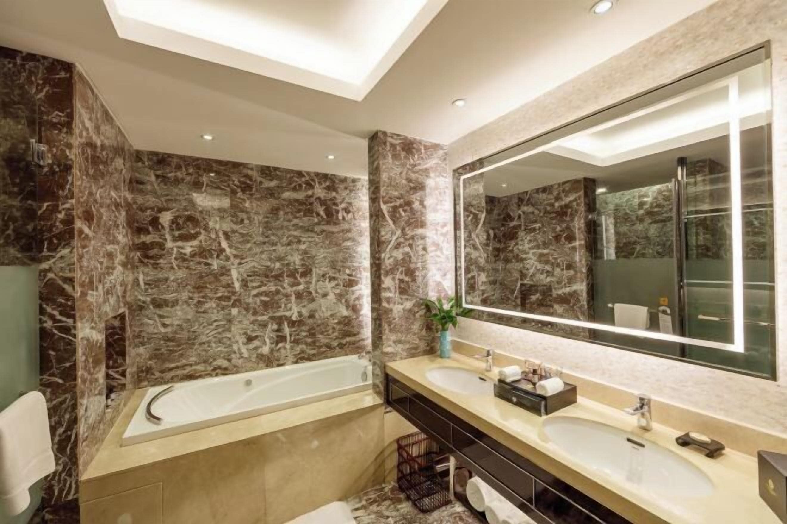 A modern bathroom with a large mirror, two sinks, a bathtub, and marble walls.