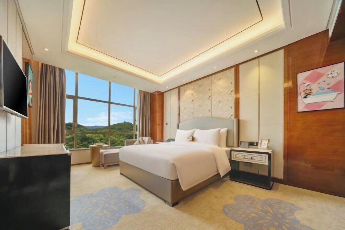 A modern hotel room with a large bed, a TV, a nightstand, and a view of the outdoors.