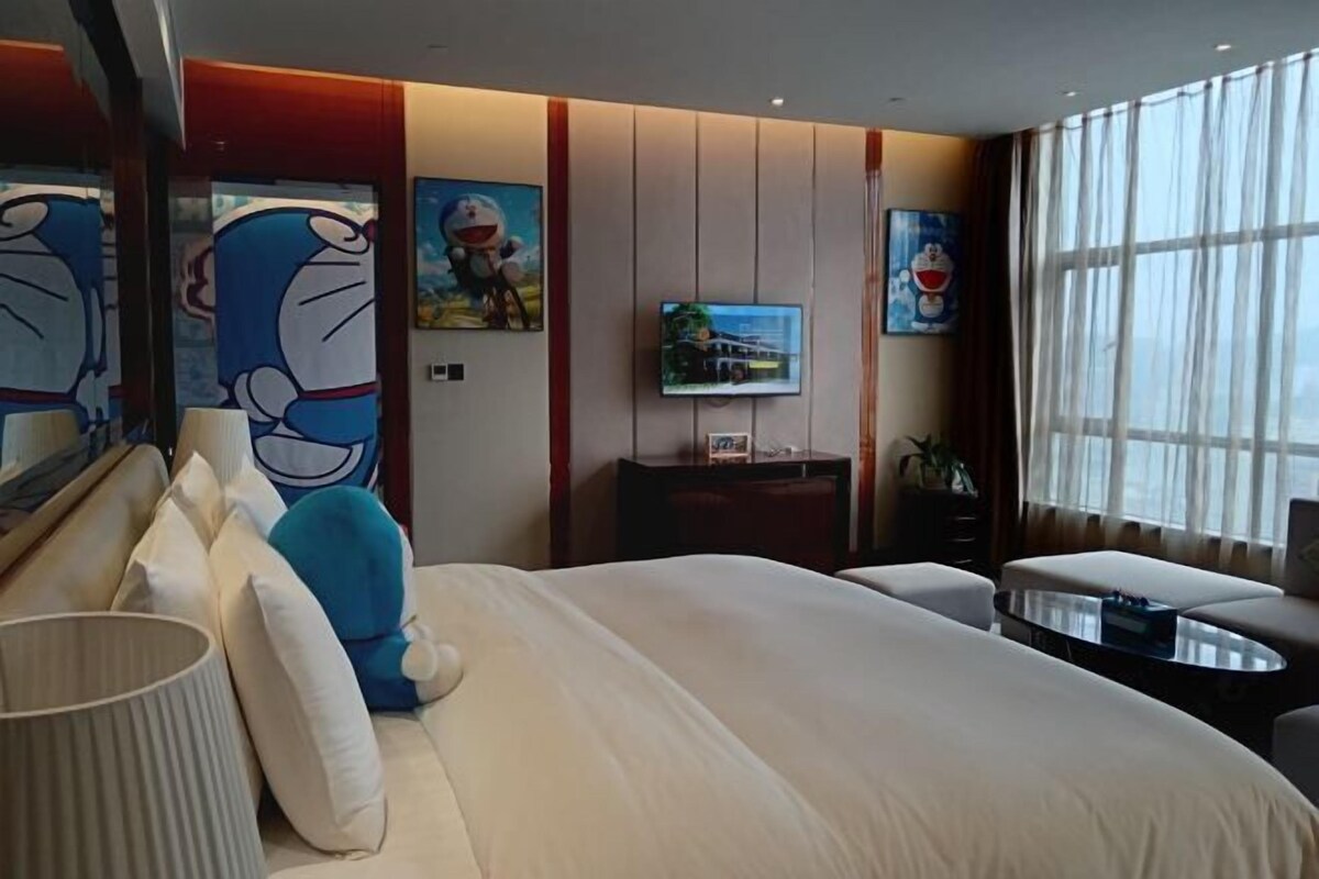 A hotel room with a large bed, a TV, a desk, and a window with curtains.