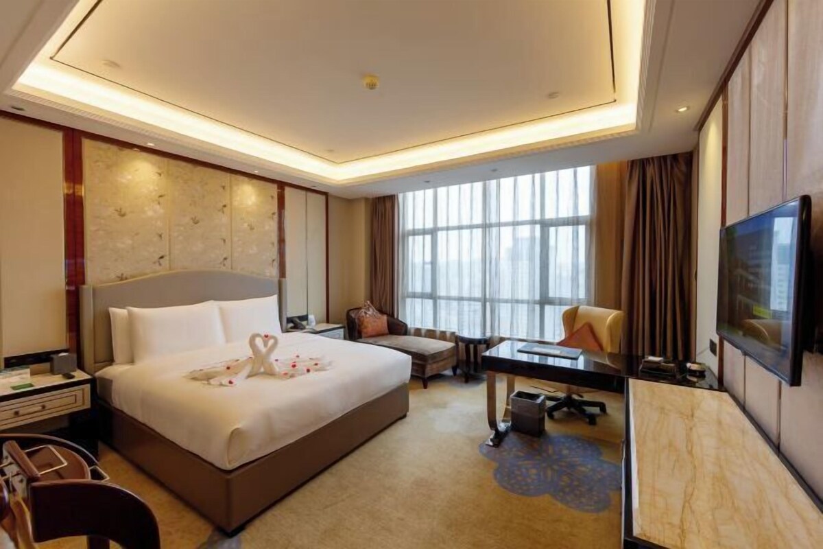A hotel room with a large bed, a desk, a chair, a TV, and a window with curtains.