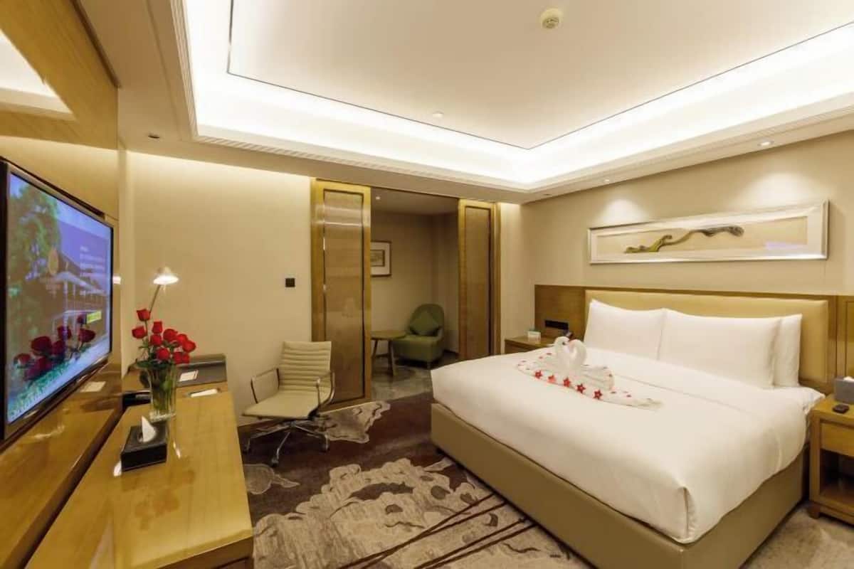 A hotel room with a bed, a television, a desk with a vase of flowers, a chair, and a small table.