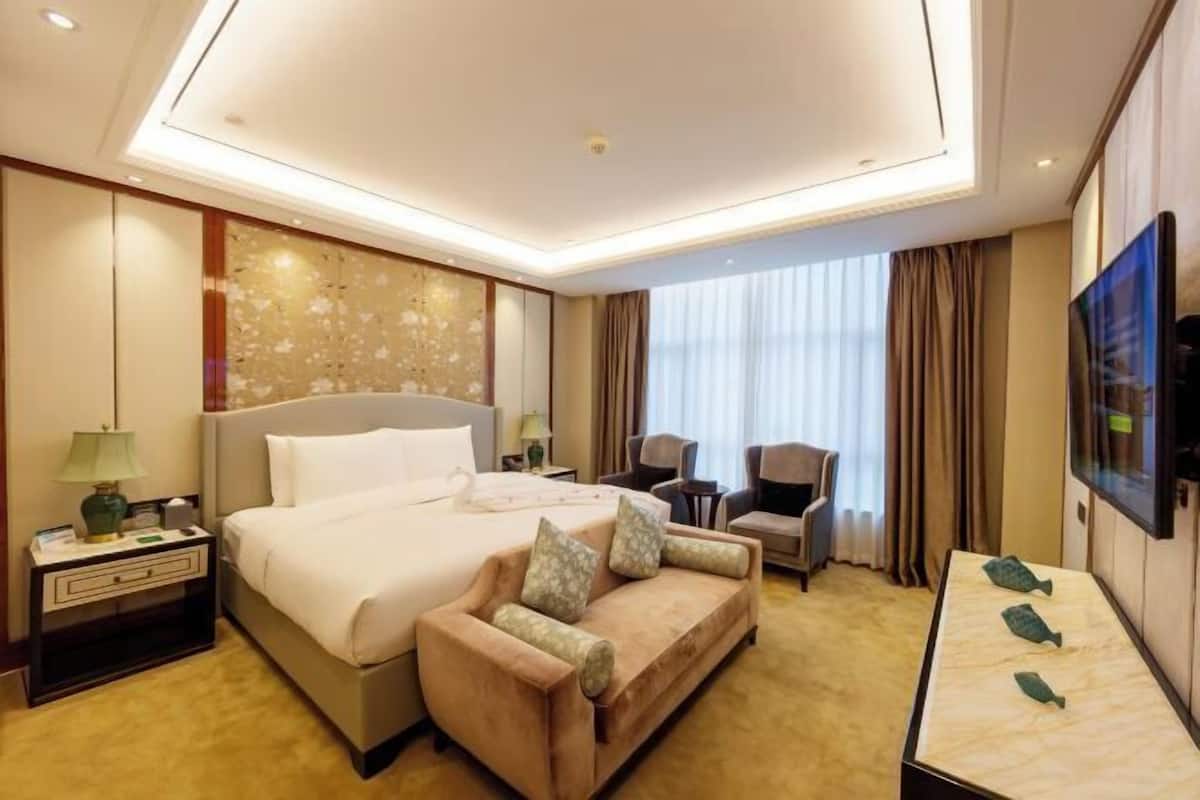 A hotel room with a bed, a sofa, a TV, a desk, and a window with curtains.