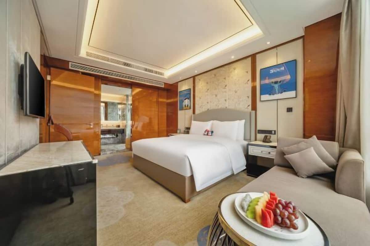 A hotel room with a bed, bedside table, TV, and a fruit plate.