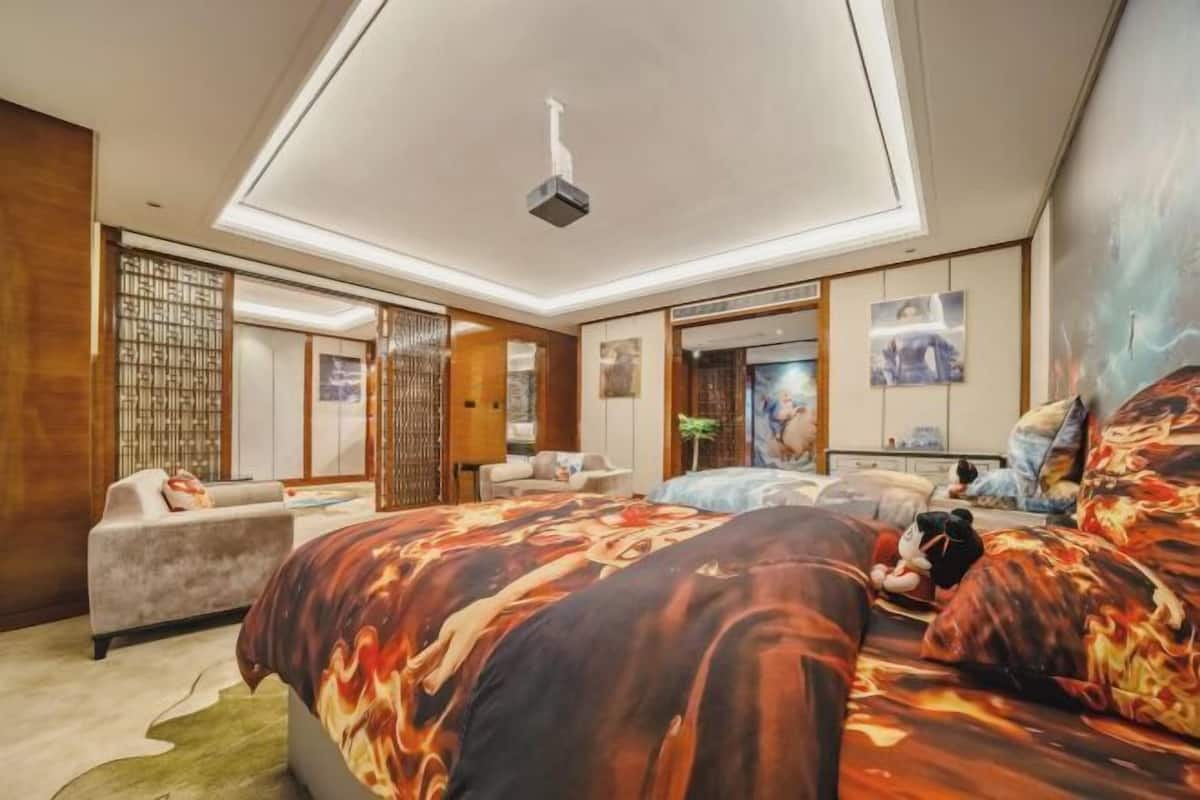 A modern bedroom with a large bed, a sofa, a desk, and a ceiling projector.