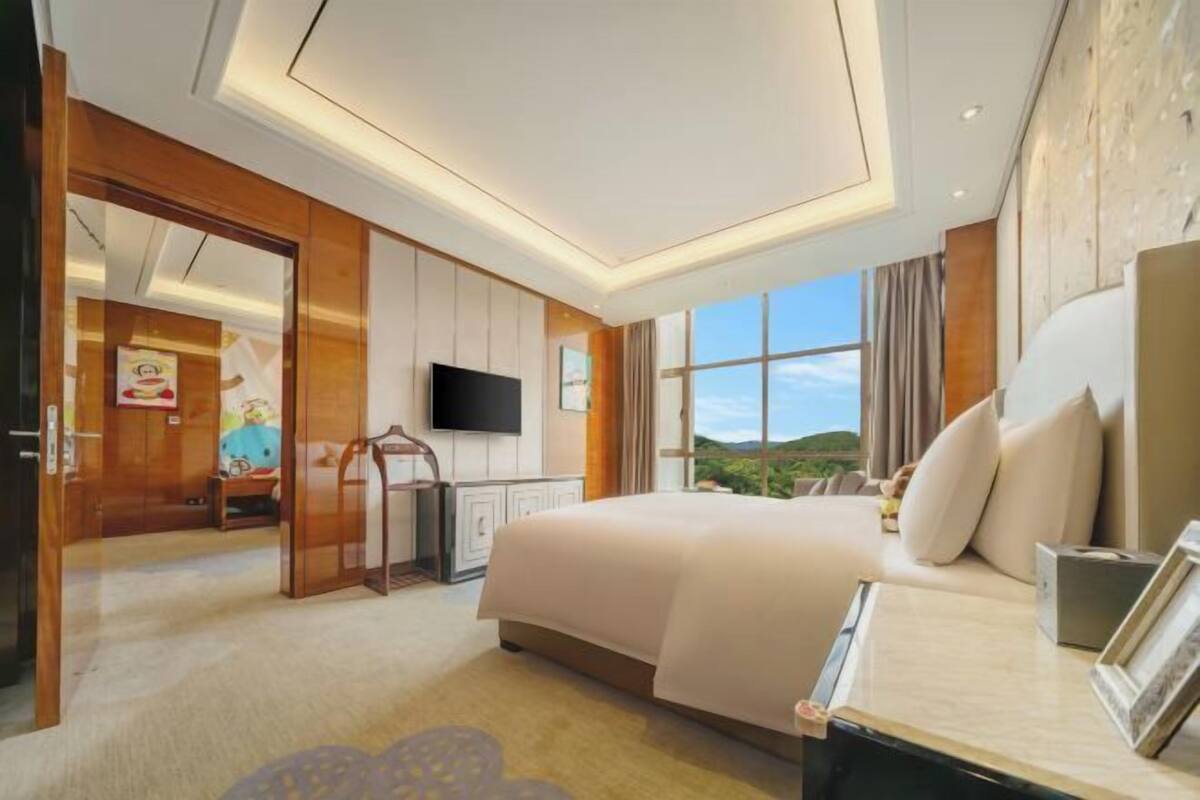 A modern hotel room with a large bed, a television, a desk with a chair, and a view of the outdoors.