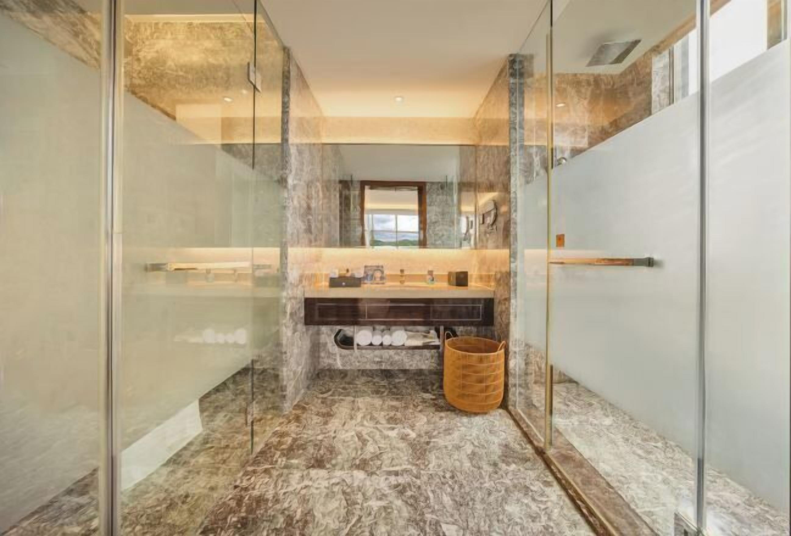 Ein modernes Badezimmer mit einer gläsernen Duschkabine, Marmorboden, einem Holzkorb und Blick durch das Glas.