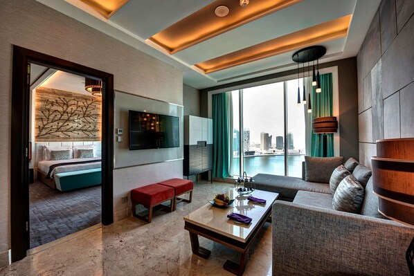 Una habitación de hotel moderna con sala de estar, una mesa de comedor, un sofá, un televisor y vistas de la ciudad.