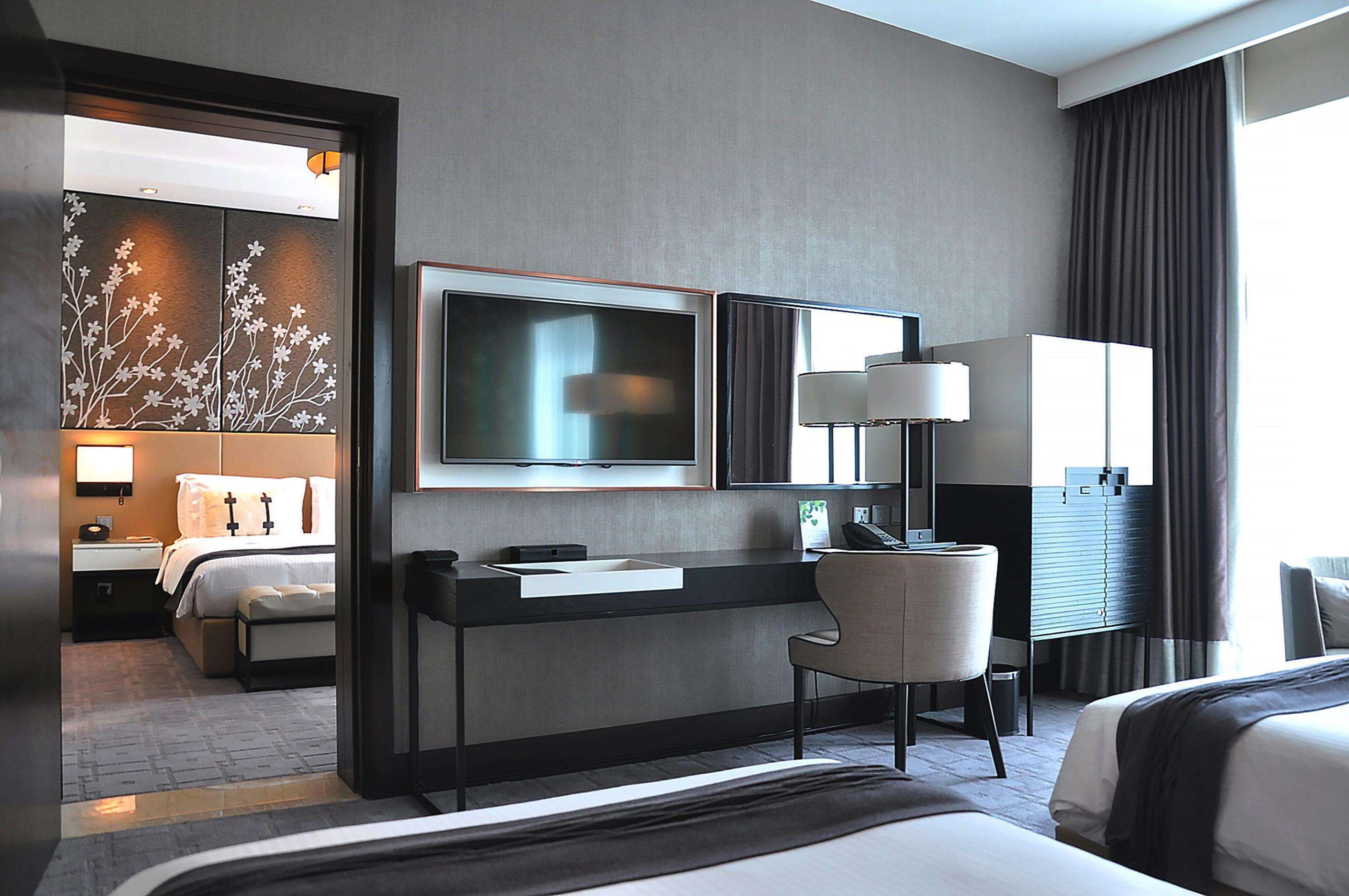 Ein modernes Hotelzimmer mit einem großen Bett, einem Schreibtisch, einem Flachbildfernseher, einem Sessel und einem Kleiderschrank.