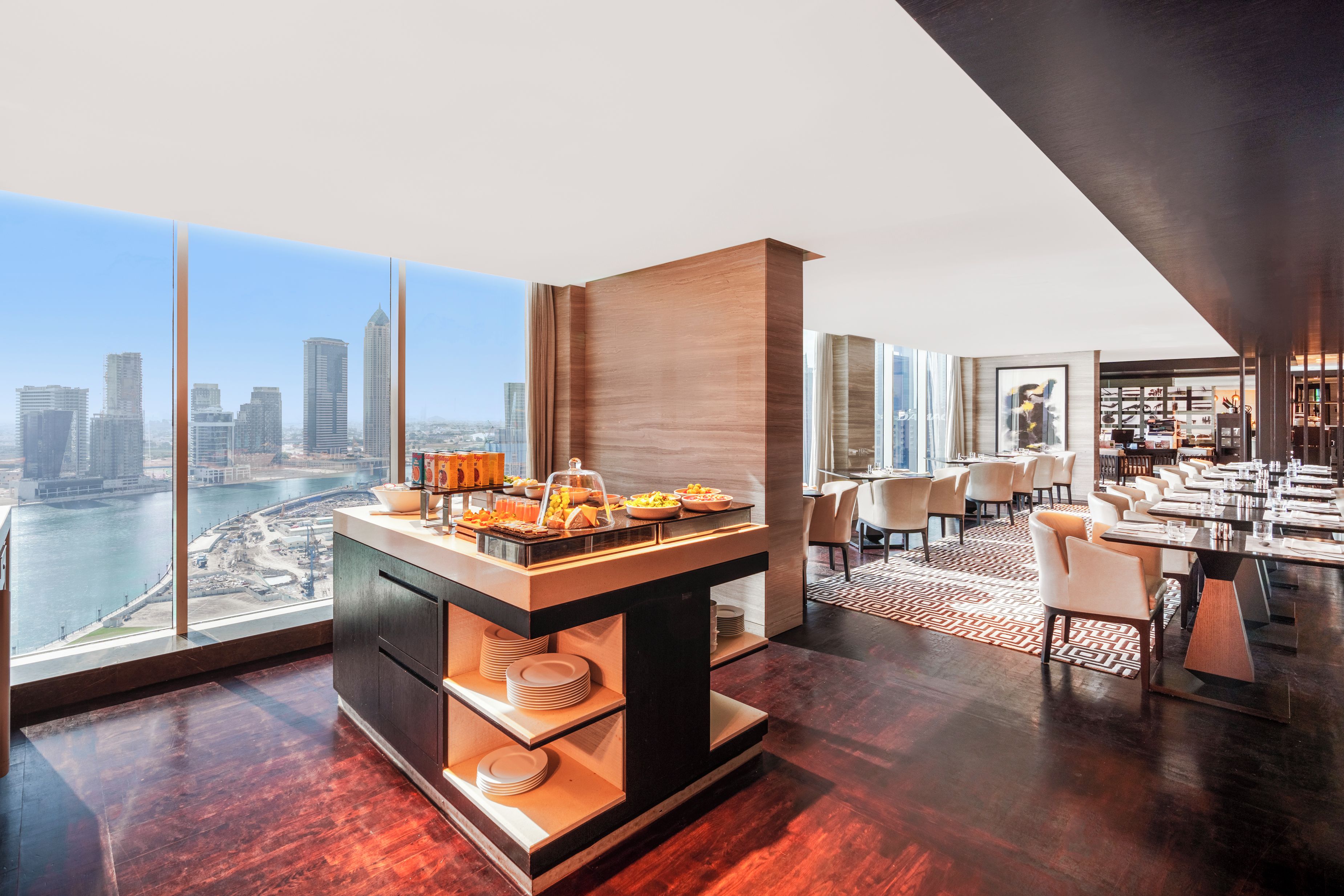 A modern hotel room with a breakfast bar, dining area, and a city view.