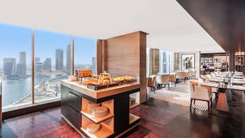 A modern hotel room with a breakfast bar, dining area, and a city view.