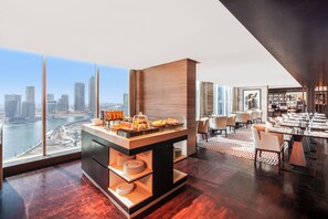 A modern hotel room with a breakfast bar, dining area, and a city view. - Pullman Dubai Downtown (Dubai)