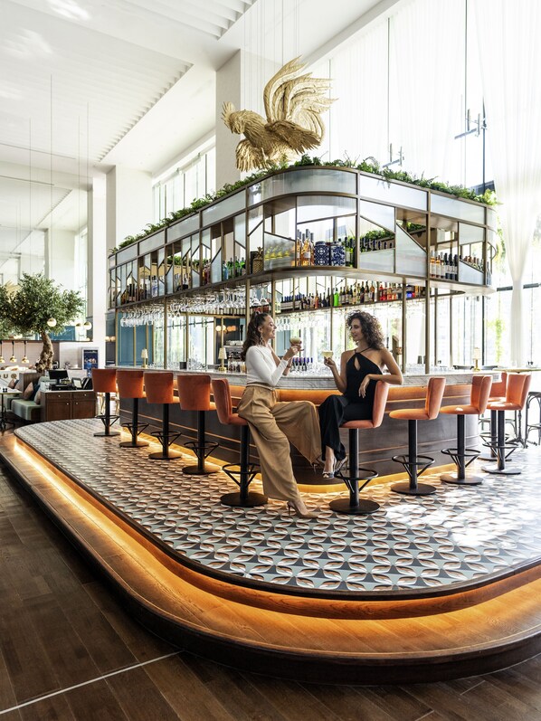 A modern bar area with a curved counter, multiple seating options, and a decorative golden rooster sculpture. - Pullman Dubai Downtown (Dubai)