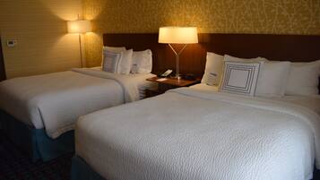Quarto de hotel com duas camas, cada uma com colcha branca, mesa de cabeceira com luminária e telefone fixado na parede.