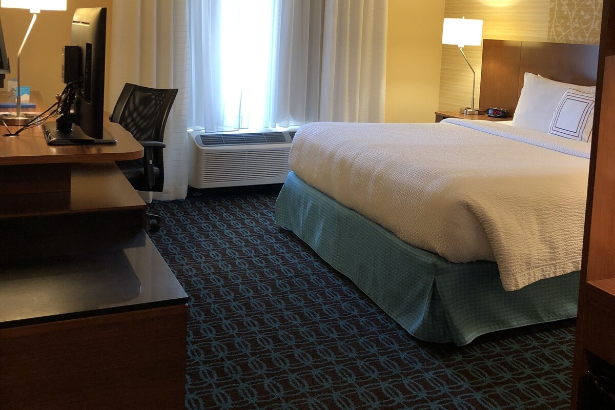 A hotel room with a bed, desk, chair, and two bedside lamps.