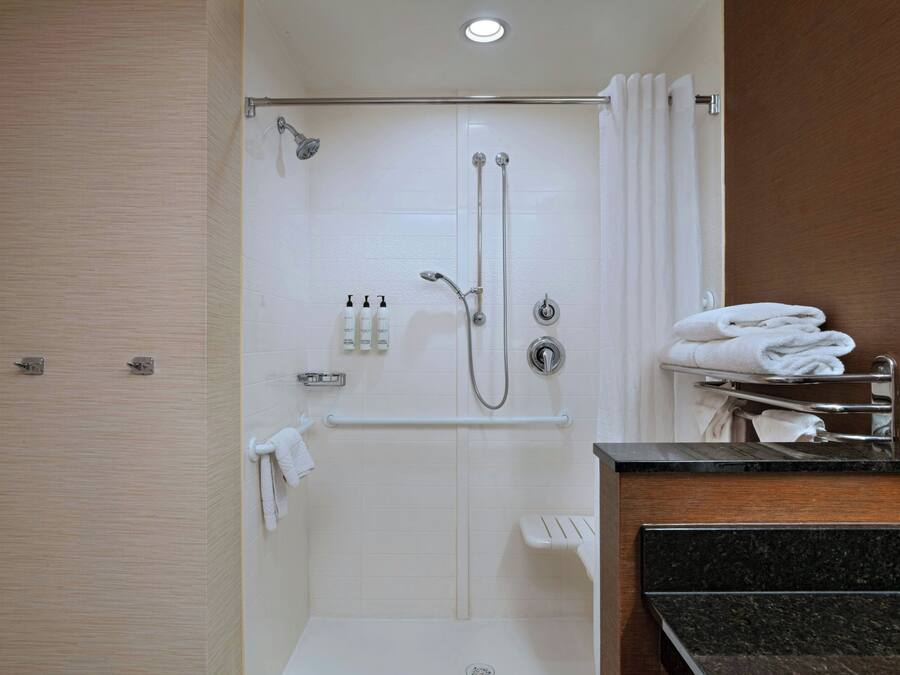 A modern bathroom with a walk-in shower, a vanity with a black countertop, and neatly folded towels on a rack.