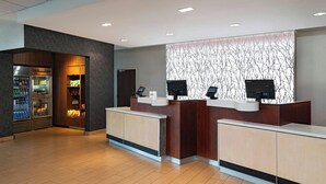 Un espace d’accueil au design moderne, comprenant un comptoir de réception, un réfrigérateur rempli de boissons et un mur orné d’un motif représentant une branche d’arbre.