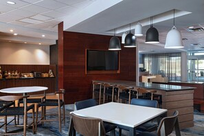 A modern hotel lobby with a bar area, seating arrangements, and a large TV screen.