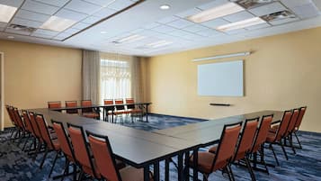A conference room with a long table, multiple chairs, a projector screen, and a carpeted floor.