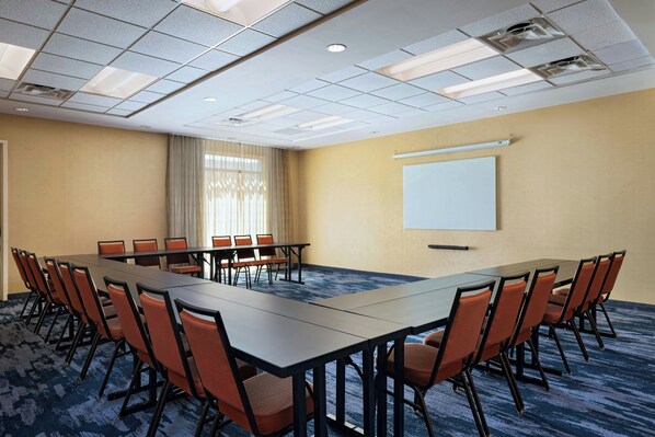 A conference room with a long table, multiple chairs, a projector screen, and a carpeted floor.