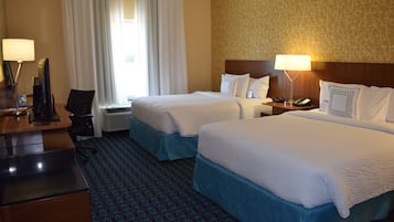 Quarto de hotel com duas camas, uma escrivaninha, uma cadeira, abajur e um telefone.