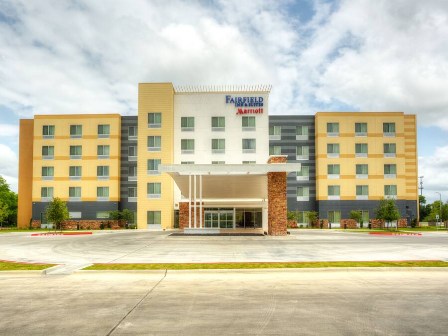 Un hotel Fairfield Inn & Suites by Marriott con un diseño moderno, que presenta una entrada central con pasillo cubierto, varios pisos y un estacionamiento al frente.