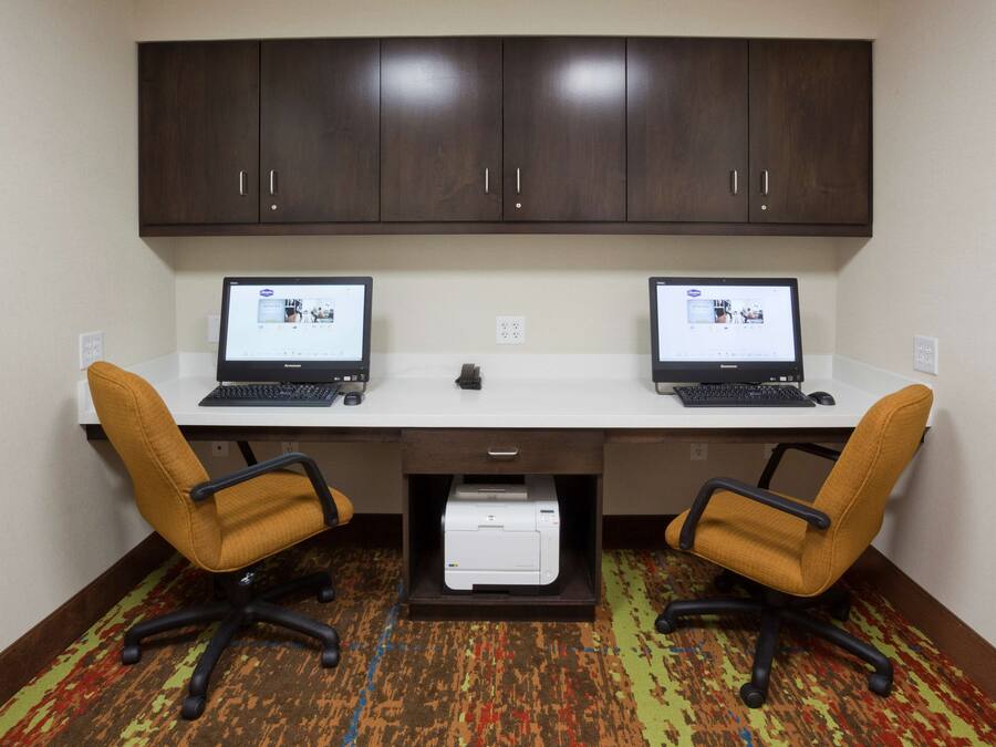 A workspace with two desks, each with a laptop, two office chairs, a printer, and a cabinet above.