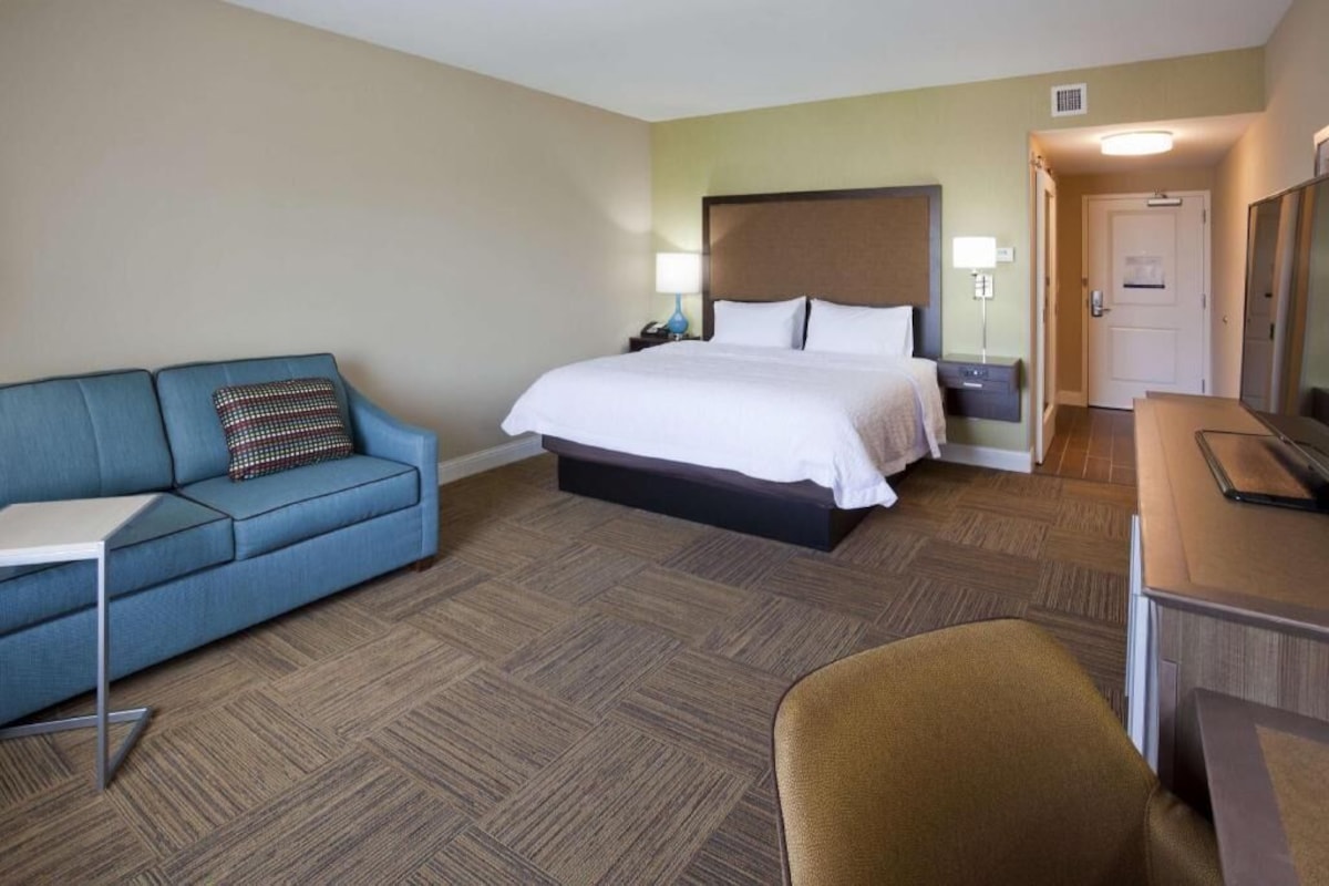 A hotel room with a bed, a blue sofa, a desk, and a chair.