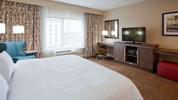 A hotel room with a large bed, a desk with a TV, a chair, and a red bench.