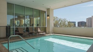 Un área de piscina interior moderna con paredes de vidrio transparente, sillones de descanso y vistas a la ciudad.