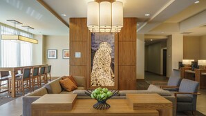 Un moderno vestíbulo de hotel con un mostrador de recepción de madera, asientos cómodos y una gran pieza decorativa en la pared.