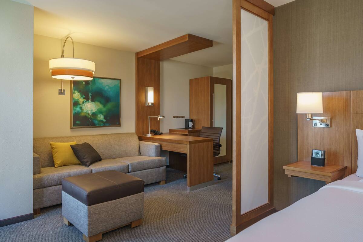 A hotel room with a sofa, ottoman, desk, and a bed.