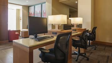 A hotel room with a desk, two office chairs, a large flat-screen TV, a keyboard, and two lamps.