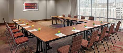 A conference room with long tables, chairs, and a large window with curtains.